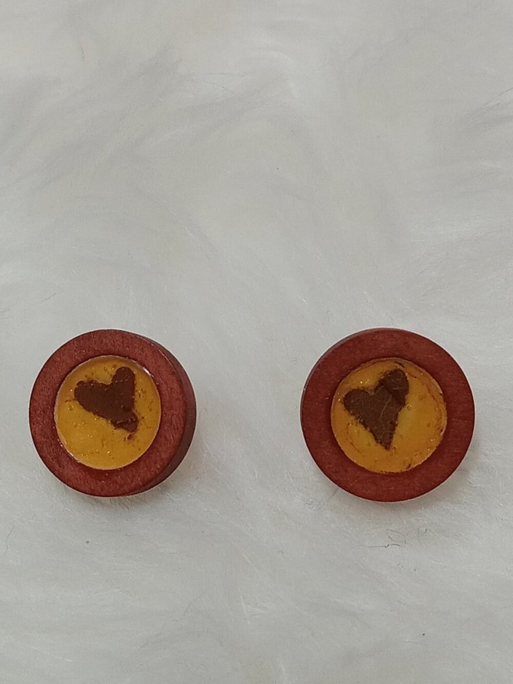 Handmade earrings on a wooden base with a piece of punched-out tree leaf